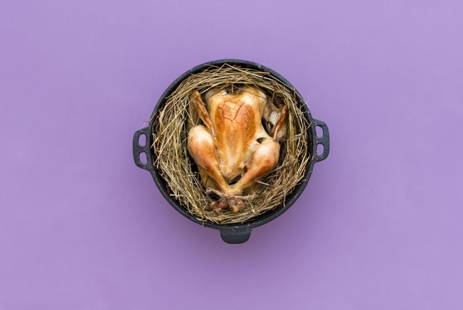 Chicken baked in the hay in an iron cast pot, top view on a purple table