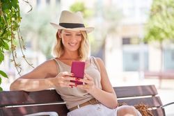 Happy stylish woman using smartphone on bench at street