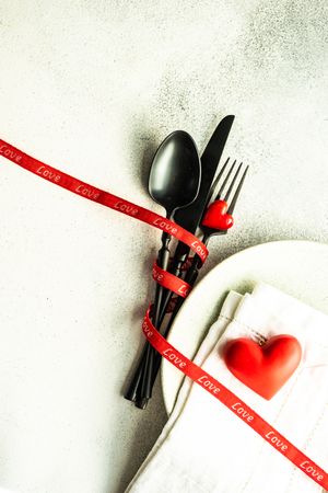 Table setting with heart decorations, ribbon and dark cutlery