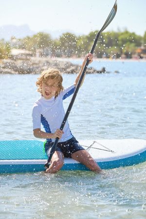 Happy boy swimming on paddleboard and screaming