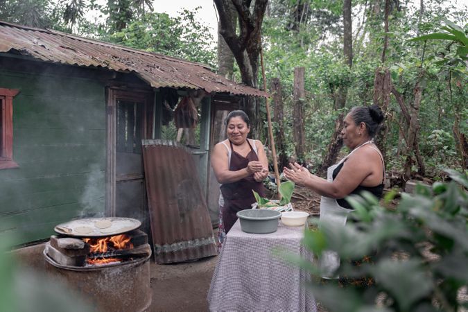 Two adult Hispanic women are shaping corn tortillas by hand