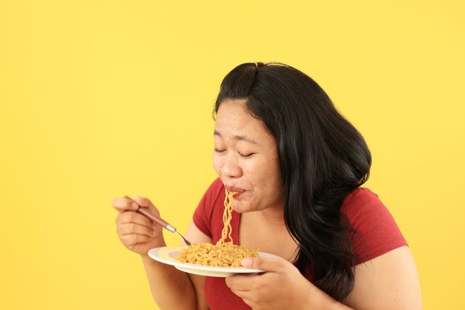 Asian Woman in Red Shirt Eating Fried Noodles from Plate with Fork