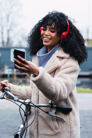 Delighted Black woman with smartphone on bicycle