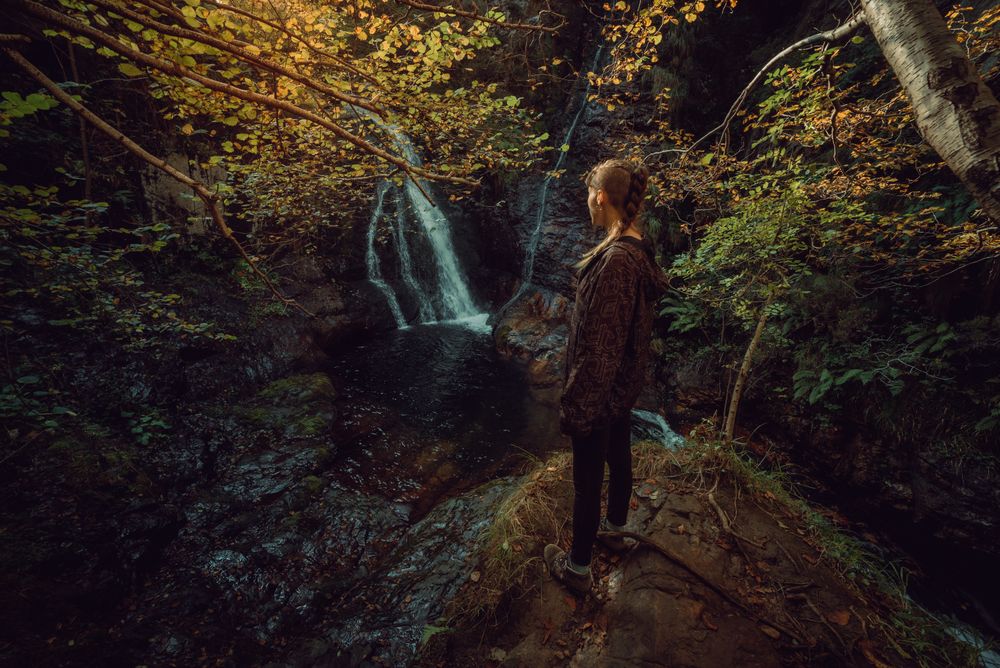 woman standing in a Small river and waterfall flowing in green dark beautiful forest.