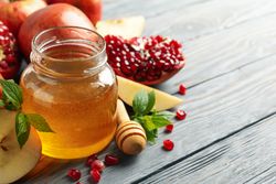 Pot of honey surrounded by slices apples and pomegranate on grey table with text for space