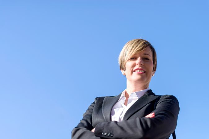 Happy proud businesswoman standing with arms crossed against blue sky