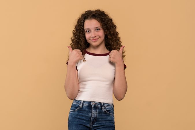 Young girl giving thumbs-up gesture, smiling confidently