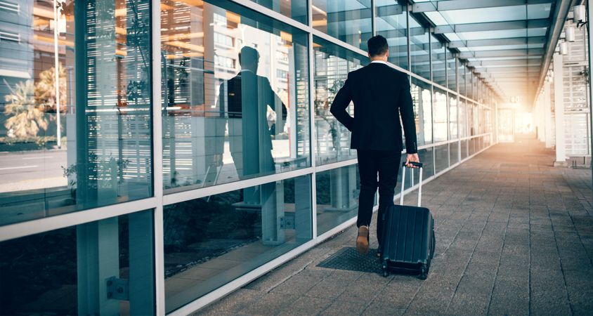 Business traveler pulling suitcase in modern airport terminal