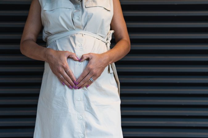 Anonymous Black woman showing heart gesture on pregnant tummy