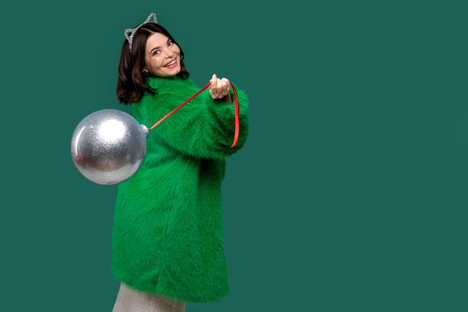 Woman in green coat smiles while holding silver holiday ornament.