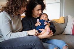 Two new moms on sofa holding their surprised baby