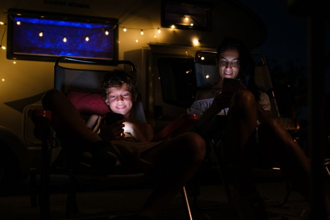 Mother and son using smartphones outside trailer at night