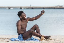 Man sitting on beach taking selfie with his cellphone