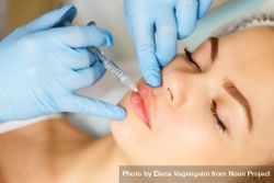 Hands in latex gloves injecting beauty treatment into upper lip 0vpkp4