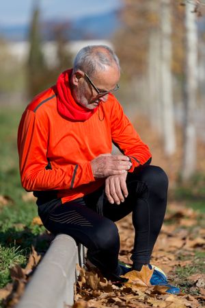 Older male sitting in park checking phone between workouts