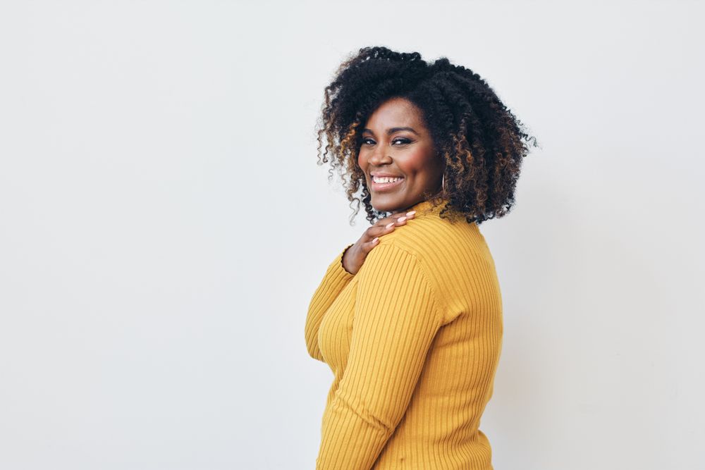 Studio shot of a confident Black woman in yellow shirt with her hand on her shoulder