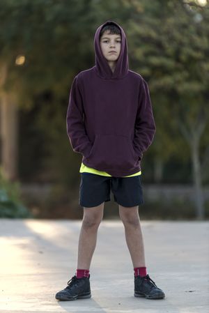 Teen boy in hoodie standing in park with trees