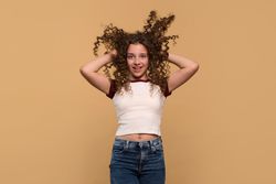 Playful young girl lifting hair with both hands, smiling energetically