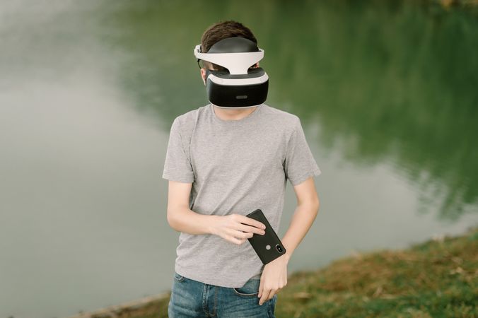 Young teenager with virtual reality glasses and smart phone outdoors