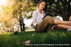Woman sitting on grass with a coffee reading book 0gQB74