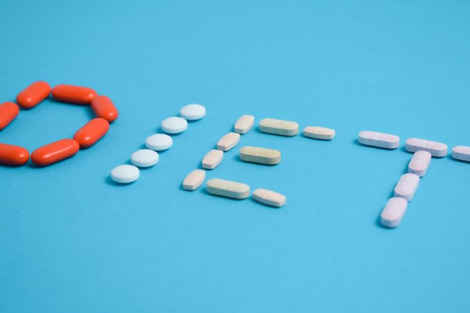 Multiple pills spelling the word "DIET" on blue background