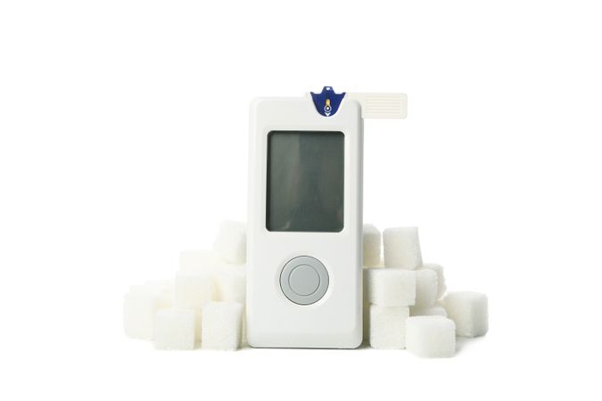 Blood glucose meter and sugar cubes isolated on light background