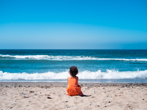 Little girl sitting on beach and admiring view