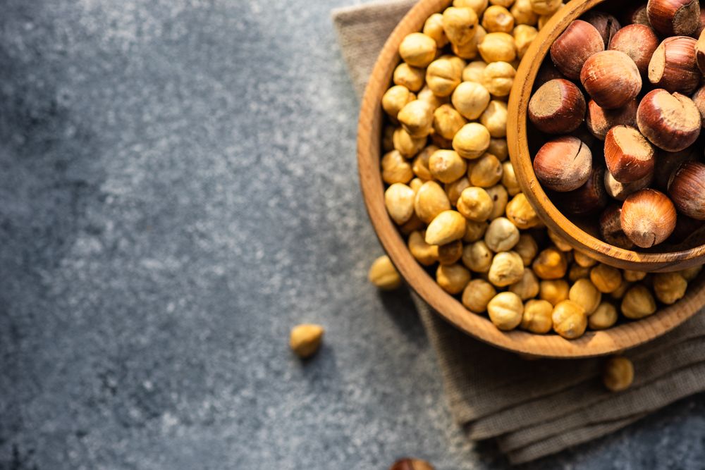 Top view of two bowls of blanched and unblanched hazelnuts