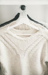 Close up of knitted sweaters on hangers, light background, vertical composition