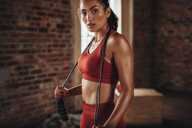 Young athletic woman standing with jump rope in gym studio