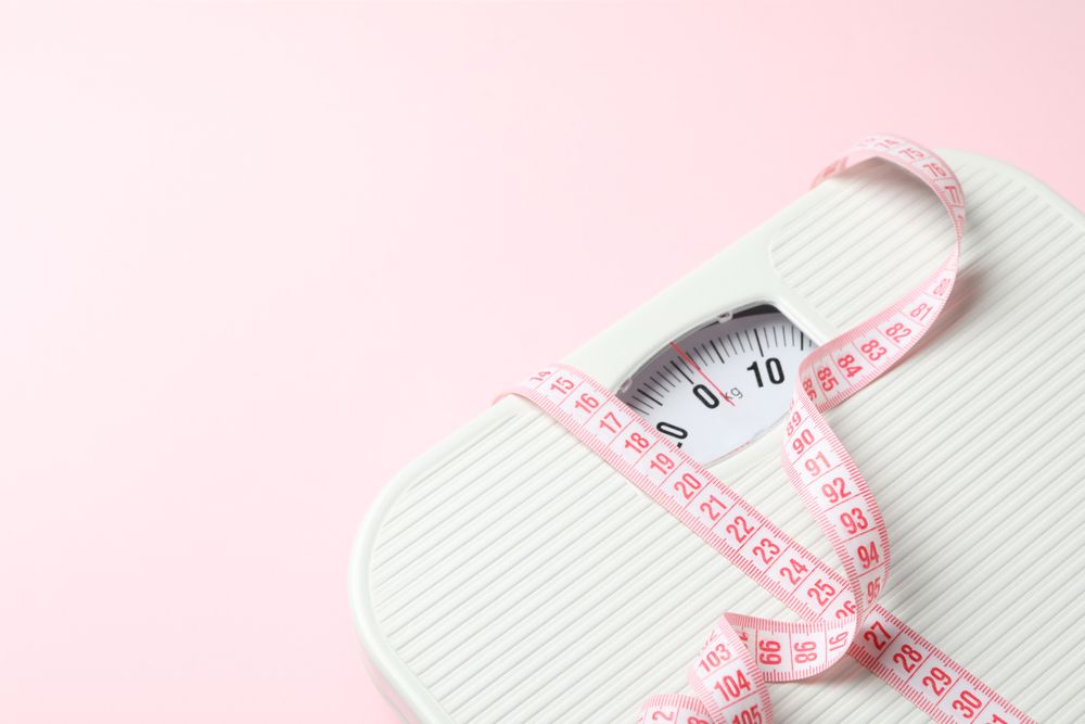 Scales and measuring tape on pink background. Weight loss concept