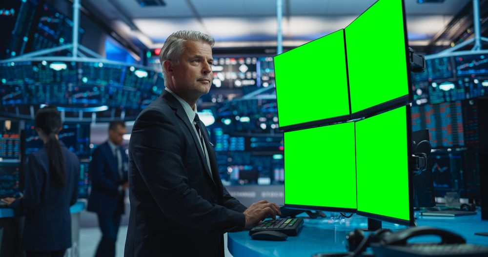 Financial Analyst Using a Desktop Computer with Multi-Monitor Workstation with Green Screen Chromakey On Display.