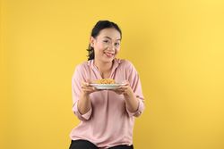 Asian Young Woman in Peach Shirt Holds a Plate of Mie Goreng Noodles with Happy Face.