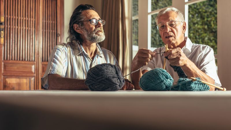 Man doing knitting with his friends looking on