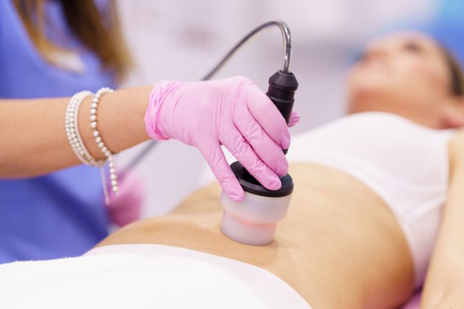 Professional in scrubs performing cosmetic procedure on stomach of woman