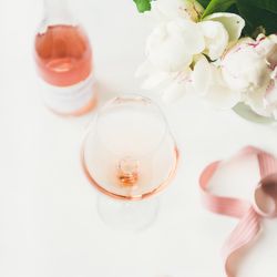 Glass of pink rose wine, and bottle with flowers and ribbon, square crop