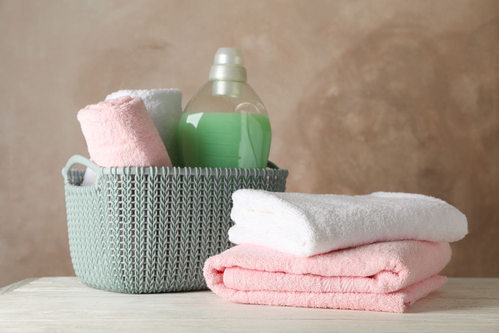 Basket with clean towels and laundry liquid on wooden background, space for text