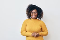 Studio shot of a smile Black woman in yellow shirt with her hands clasped in front of her