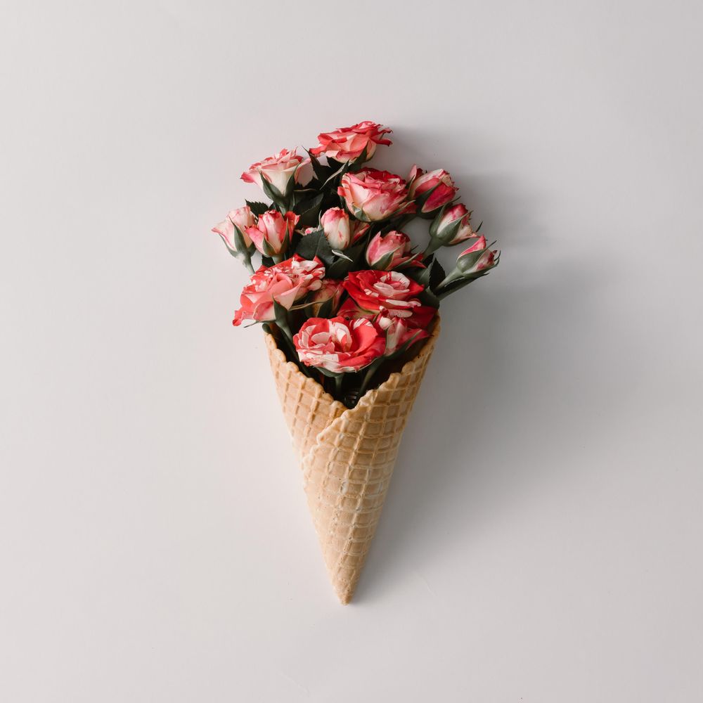 Ice cream cone with colorful flowers on light background