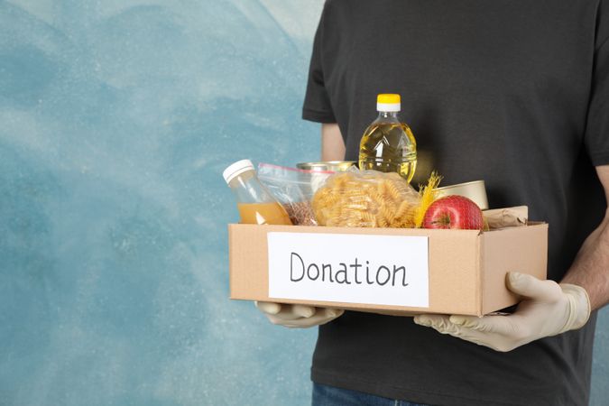 Young man holds donation box against blue background. Volunteer