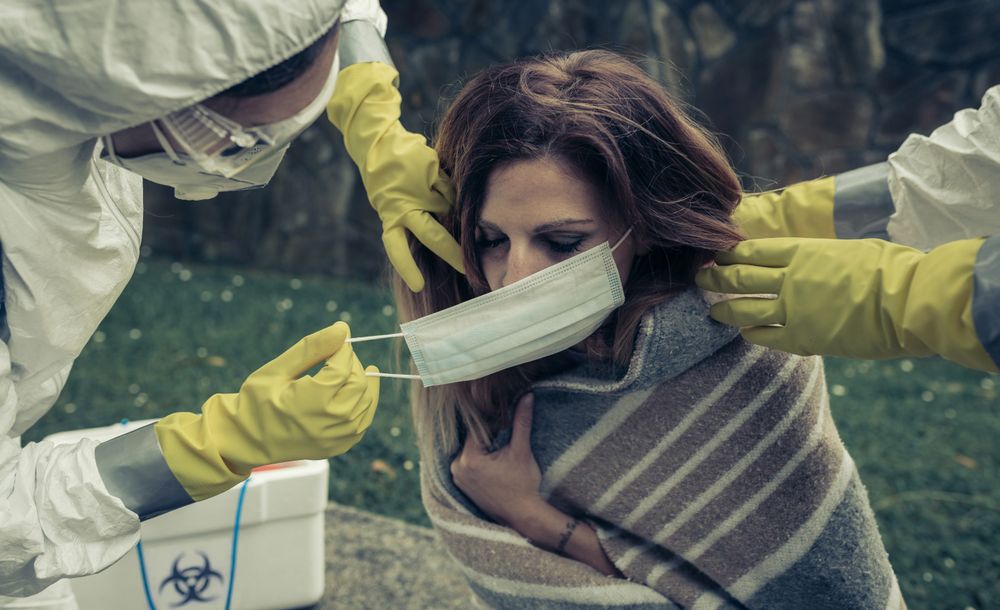 People in bacteriological protective suits putting a mask on woman
