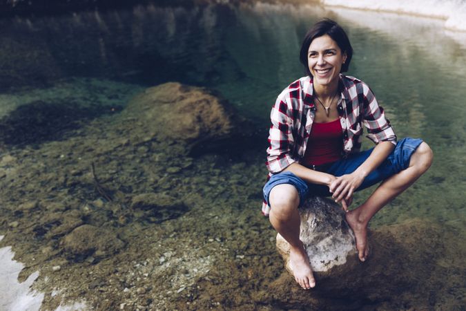 Cheerful woman sitting on rock in clear water