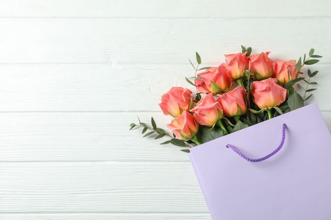 Gift bag with bouquet of pink roses on light background, space for text