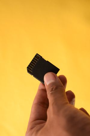 Hand holding SD card for data with yellow background