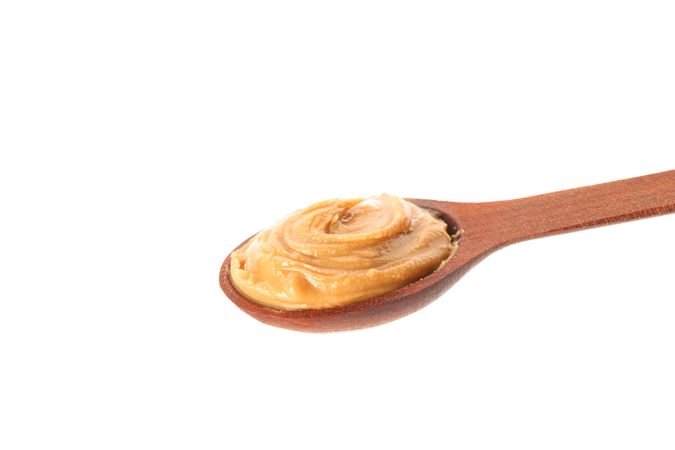 Creamy peanut butter in wooden spoon isolated on bright background, closeup. A traditional product of American cuisine