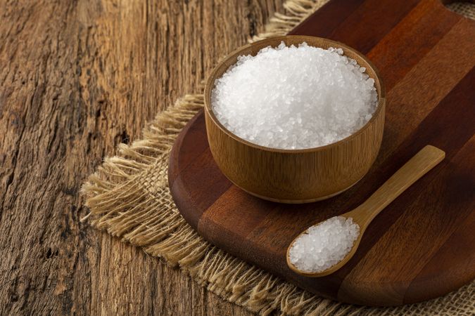 Coarse salt in bowl on wooden background.