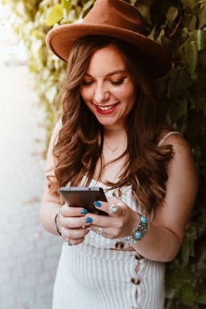 Woman in hat smiling browsing smartphone