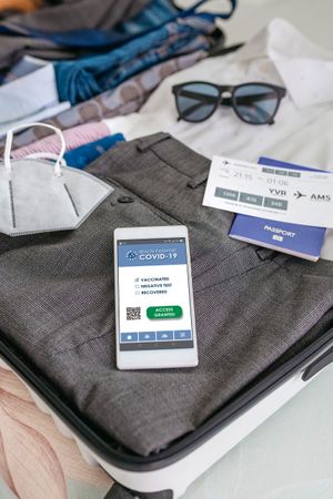 Businessman suitcase prepared for business trip with covid passport on mobile
