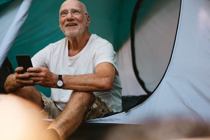 Smiling mature man sitting in tent with his mobile phone