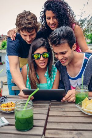 Friends sitting outside gathered around digital tablet
